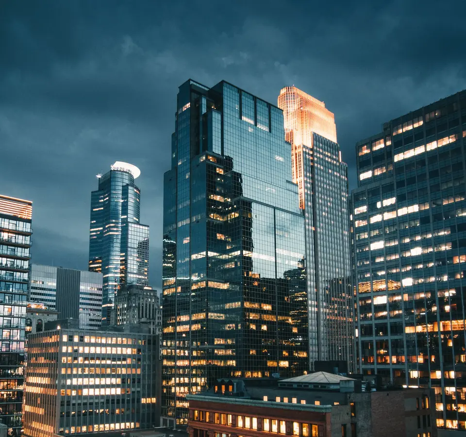 Downtown Minneapolis at dusk, glass towers and a gold-lit crown rising above rows of lit office windows